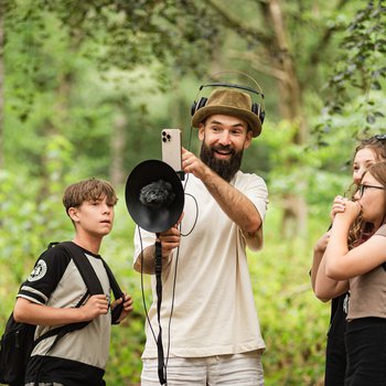 Three people in a woodland gathered around a man with recording equipment