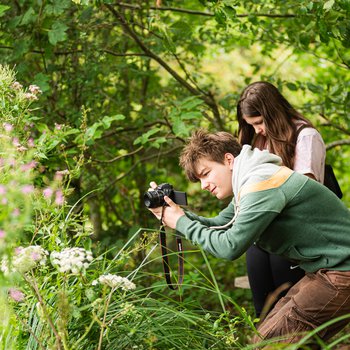 Two young people in a woodland taking photos with a camera