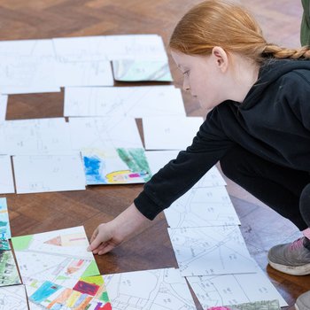 Student putting their art map on the floor along with other pieces of the map