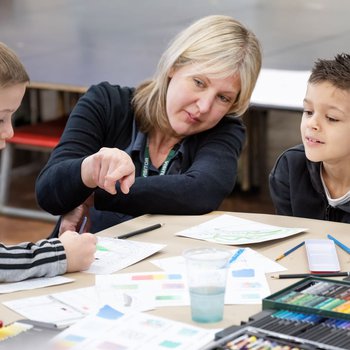 Staff member helping two students with their art maps