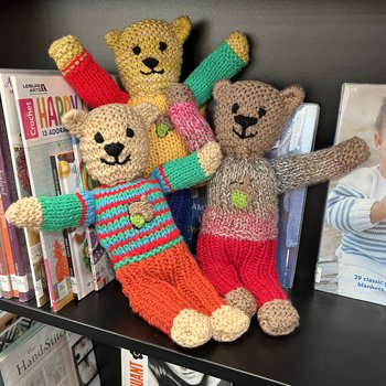 3 knitted bears on a library book shelf