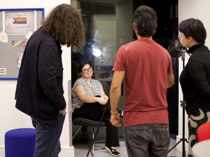 Photograph of seated individual being interviewed with camera crew in foreground