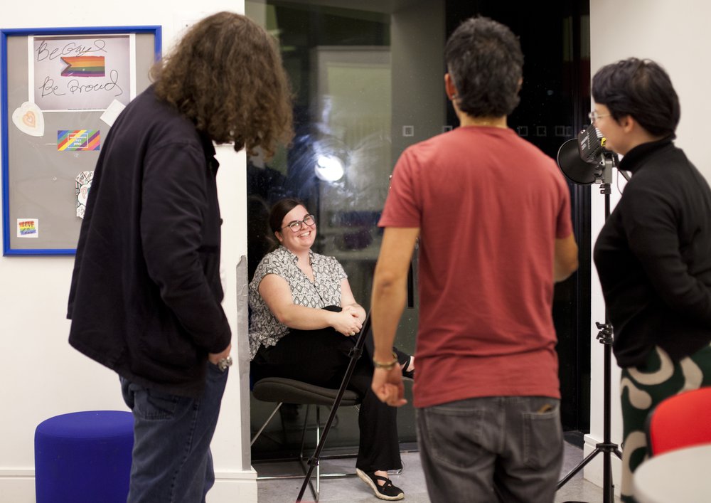 Photograph of seated individual being interviewed with three camera crew in foreground