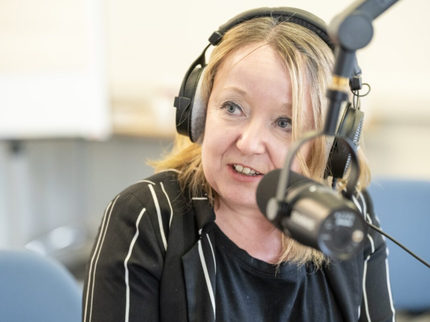Woman with blonde hair speaking into a microphone and wearing headphones