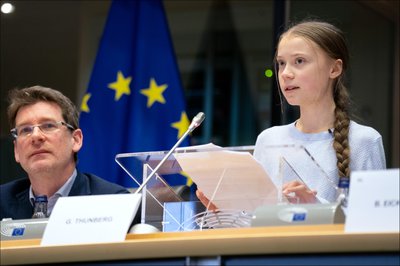 Greta Thunburg at a podium with the EU flag behind her