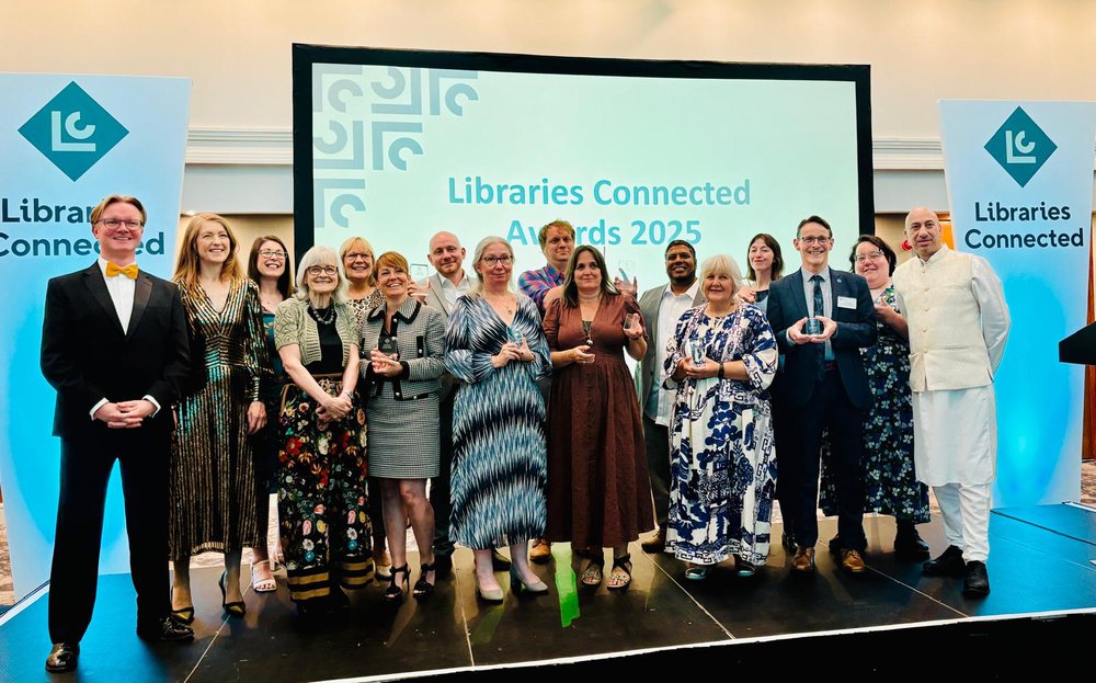 A group of people with Peter Gaw centre right, on the stage holding their awards at the libraries connected awards