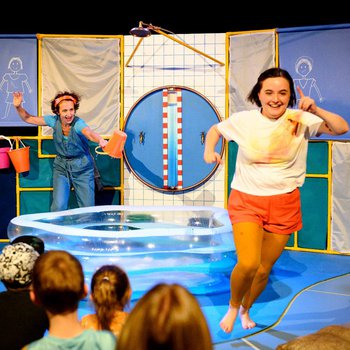 Actors run around a paddling pool on stage.