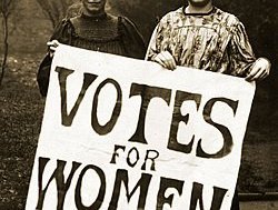 Two Suffragettes holding a large 'Votes for Women' poster