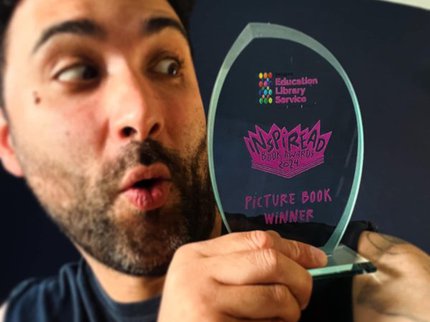 An author in a black tshirt holds a trophy