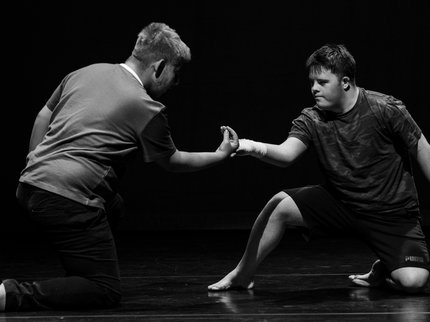 Black and white image of two boys knelt on the floor holding hands during a dance