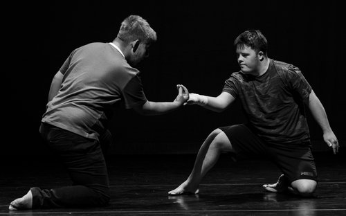 Black and white image of two boys knelt on the floor holding hands during a dance