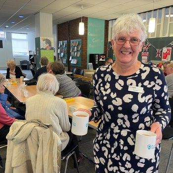 Grey haired lady holding mugs of tea in Places of Welcome group in the library