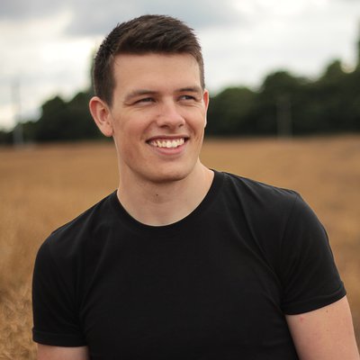 Young man standing in a field smiling wearing black t shirt