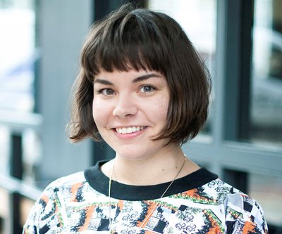 Young lady with short bob haircut smiling and wearing a patterned top and necklace