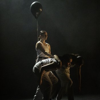 Three dancers on stage together in front of a black balloon