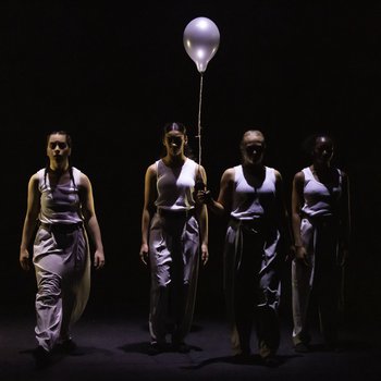 Group of four dancers standing on stage in front of a white balloon