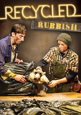 Two puppeteers, covered in dirt, are handling and looking at a dog made out of recycled components