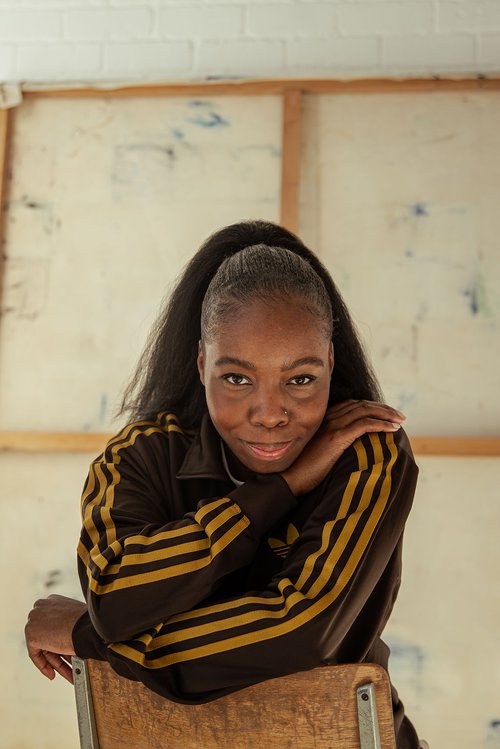 A headshot of a woman wearing a black and yellow striped top leaning over a chair.