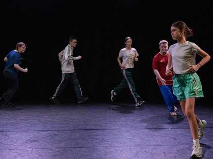 Five young dancers wearing sportswear running across a stage.