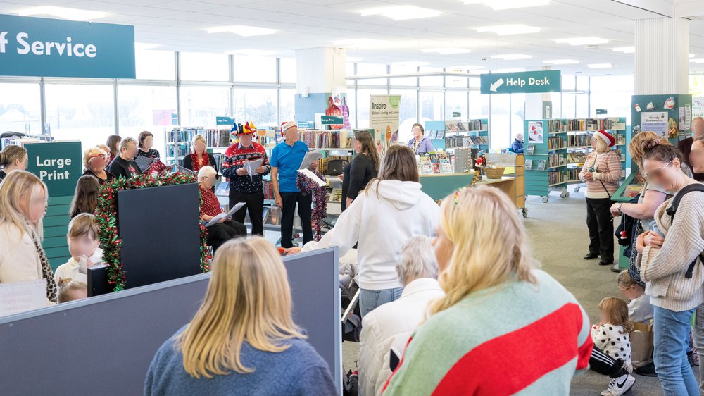 A crowd gathered in a library watching a choir perform