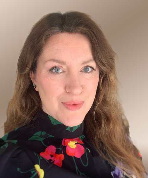 A headshot image of a woman with curly hair wearing a floral top
