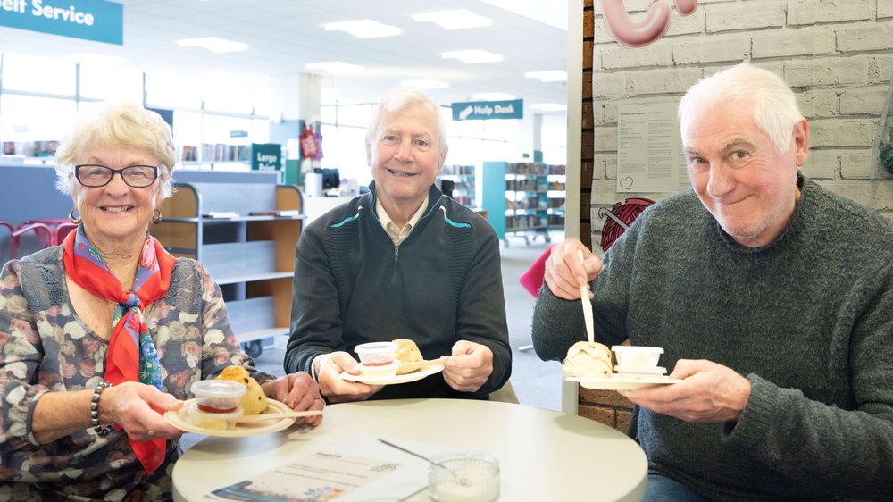 Three people sat together enjoying a scone at a library Songs and Scones event