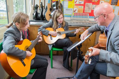 Two students being taught to play the guitar by a teacher