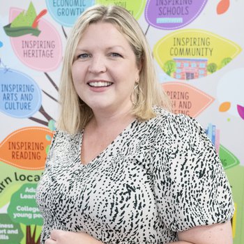 A woman in a black and white spotty dress and should length blonde hair smiles
