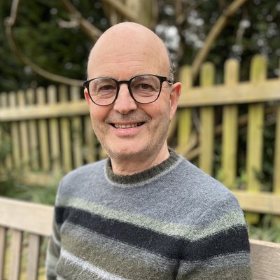 Picture of Simon Packham - author. He is a older middle-aged white man with a bald head, glasses and a grey jumper