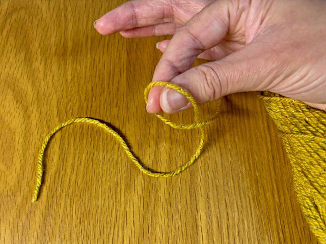 Photo of fingers reaching through a loop in a piece of yarn