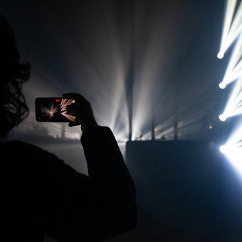 A shadow of a person with curly hair holding a mobile phone in front of strobe lighting.