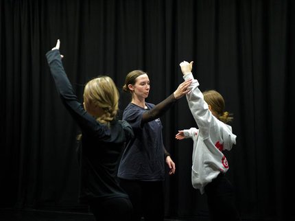 Two girls raising their left arms facing a lady raising her right arm.