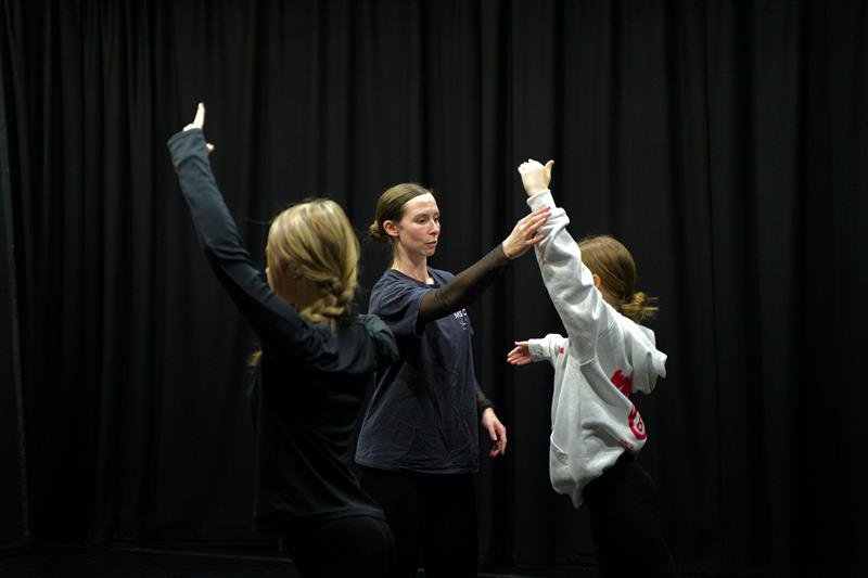 Two girls raising their left arms facing a lady raising her right arm.