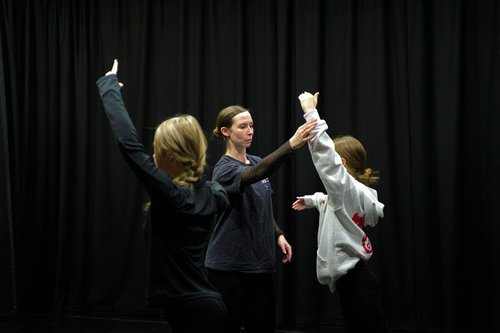 Two girls raising their left arms facing a lady raising her right arm.