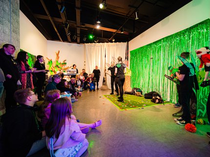 A group of young people performing a play in front of a group wearing green fairy wings