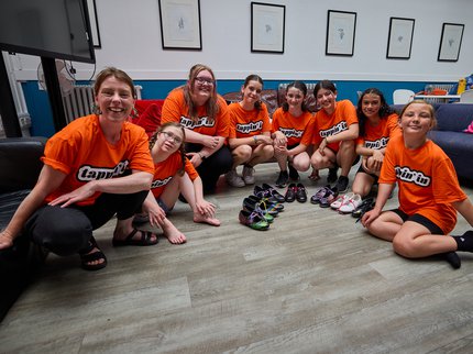 A group of 8 people wearing orange Tappin' In Tshirts sat on the floor and smiling.