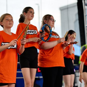 Five young people in orange T shirts holding percussive instruments.