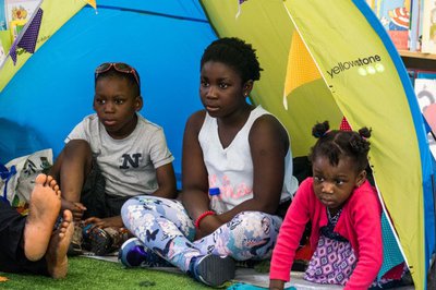 Three children sit in a blue and yellow tented pod.