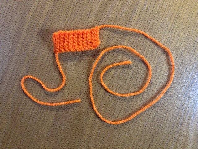 A small rectangle of knitting, with a long tail and a shorter tail of wool at opposite ends