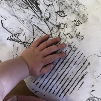 An image of a child's hand mark making on paper with graphite