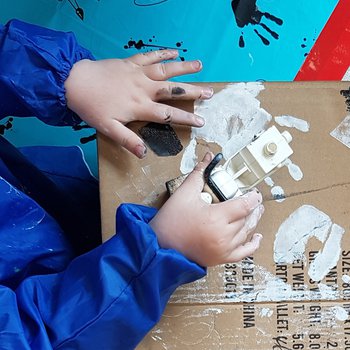 An image of child's hands painting on a cardboard box