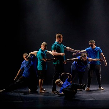 Six young dancers wearing blue t-shirts performing on stage