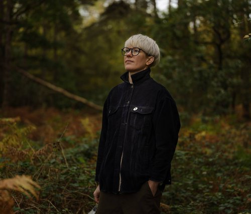 A woman with short blonde hair stood against a background of autumn leaves.