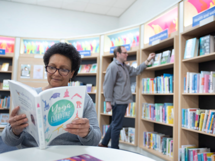 Person sat reading a book while another reader browses the shelves behind them