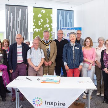 Group of volunteers male and female standing behind table with a celebration cake on it