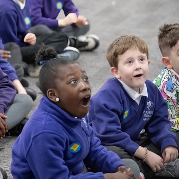 School children sit on the floor, mouths opened wide in surprise.