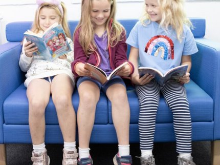 Three children sat on a blue sofa, reading and smiling