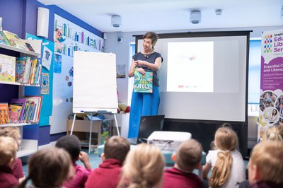 A woman holds up a book and reads to a group of children
