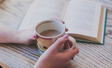 a book open on a table and somebody holding onto a mug of tea