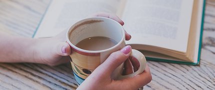 a book open on a table and somebody holding onto a mug of tea